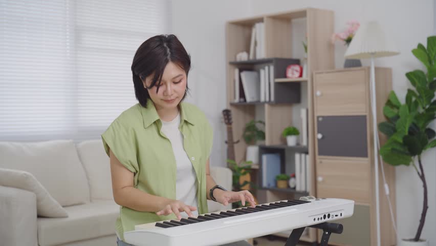 Asian Woman Playing Electronic Keyboard Piano in Living Room at Home for Music Practice Concept