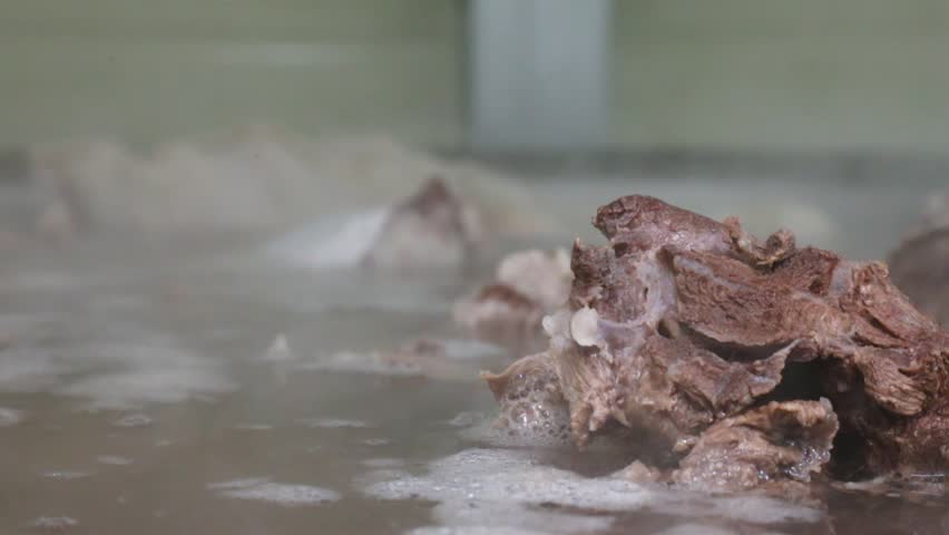 Close-up of cooked meat simmering in a large pot of broth with steam and foam