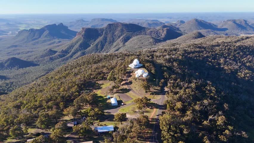 Wide aerial shot of telescope domes on a mountain ridge in Warrumbungle National Park, Australia.
