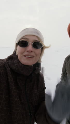 Portrait of young Caucasian couple waving and talking to camera during winter hike in snowy landscape, vertical. Clip is ideal for winter tourism ads or travel vlogging promos