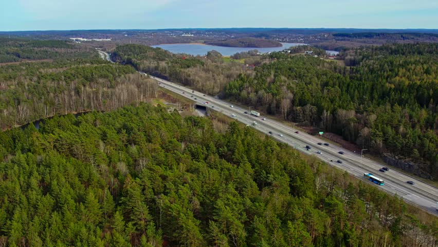 Aerial view of highway traffic passing through dense forest near lakes and hills