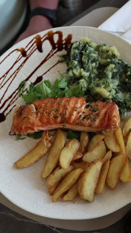 Vertical screen Grilled salmon with roasted potato wedges and creamy spinach served as a fresh Mediterranean meal at a cozy seaside restaurant