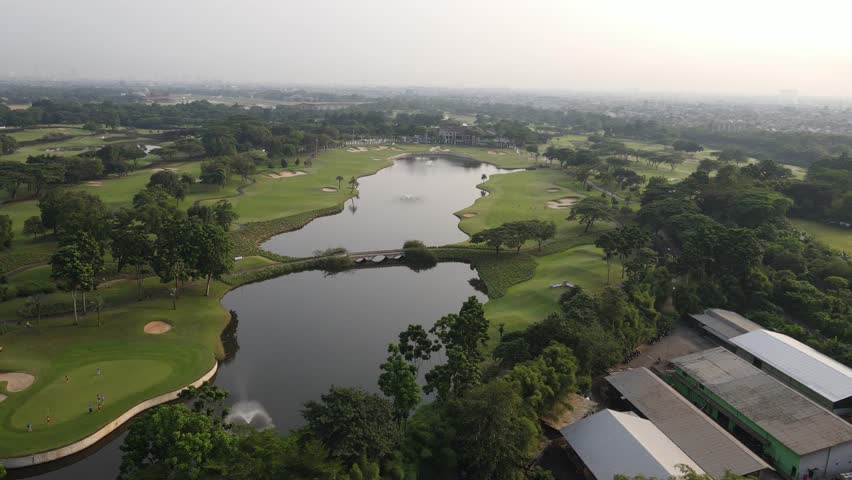 Cinematic aerial drone footage of a beautiful golf course with lush green fairways and golfers playing. Stunning aerial landscape ideal for sports, luxury lifestyle, tourism, resort, recreation, and corporate projects.