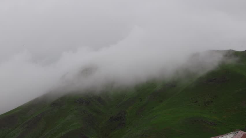 Heavy Fog and Mist Moving Across Mountain , Low Clouds Rolling Over Lush Green Mountain Face in Summer