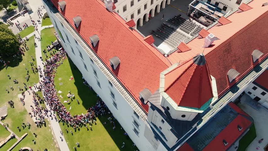 Top-down aerial drone view of visitors gathered during a historical festival at Bratislava Castle. Large crowd surrounds the castle walls during a cultural celebration in Slovakia.