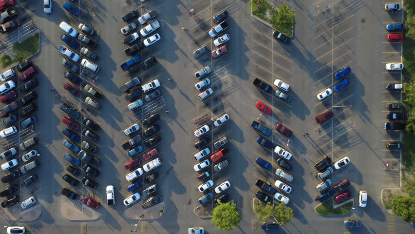 Long afternoon shadows extend across organized vehicle rows at busy West side grocery store lot along Potranco Road. Peak hour activity shows cars seeking spaces in San Antonio, Texas. USA