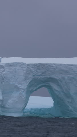 Vertical View of Iceberg and Ocean Sea Waves Breaking on Ice on Cold Misty Day