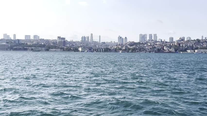 Scenic view of Istanbul city skyline and modern skyscrapers from the Bosporus strait water under a blue sky in Turkey, coastal cityscape view, seaside travel scenery, peaceful waterfront landscape.