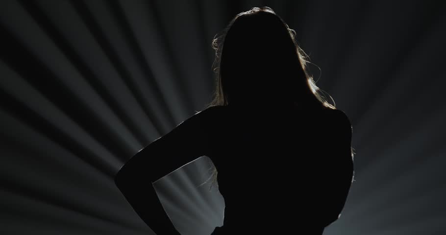 Silhouette of a female dancer performing on a dark stage, back lit by dramatic volumetric light rays with copy space. Concepts related to dance, self discovery, album covers, singles, or podcasts