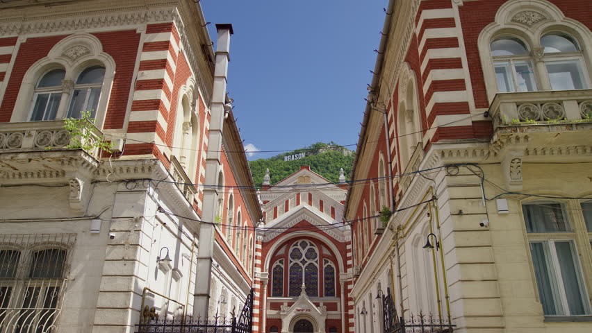 Low-angle view of Brasov red brick Beth Israel Synagogue, framed by ornate facades beneath Tampa Mountain and the city sign.