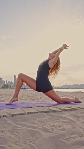 Morning yoga takes place on the beach in Benidorm. A person performs stretches and poses while the waves gently lap at the shore and the sun rises.
