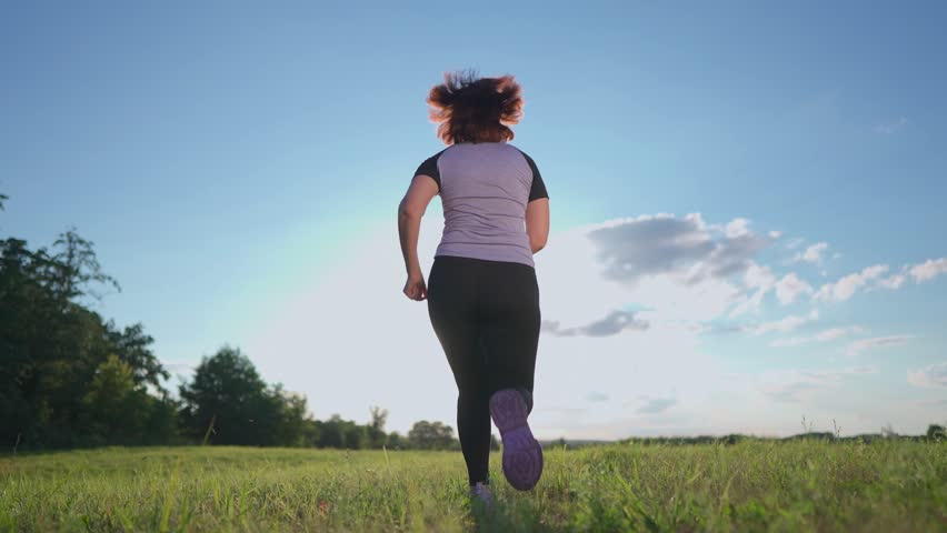 A woman jogs through an open field, embracing the sport of running. The woman enjoys her sport in a bright, sunny environment, showcasing a commitment to fitness and health.