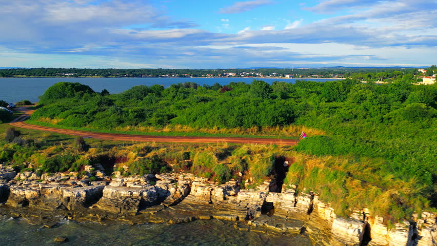 A senior adult enjoys a peaceful cycling ride along a scenic coastal path surrounded by lush greenery and rocky formations. The wide-angle shot captures the tranquility of this recreational pursuit.