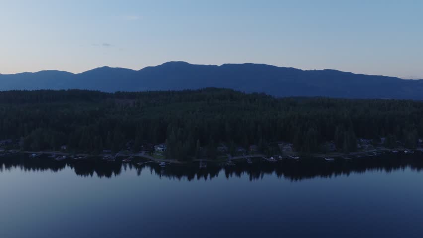 Calm water on Sproat Lake reflects forested shoreline and distant mountains at dusk