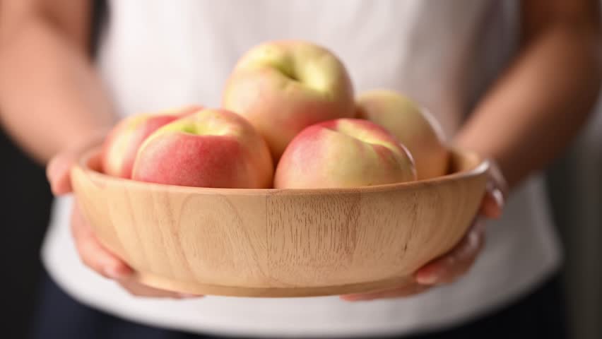 Woman hands holding a fresh organic nectarines in a wooden bowl