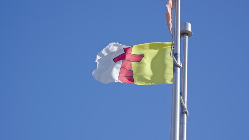 Telephoto close-up shot of the yellow, white, and red Flag of Nunavut with its central red Inuksuk flapping steadily in the Arctic wind.