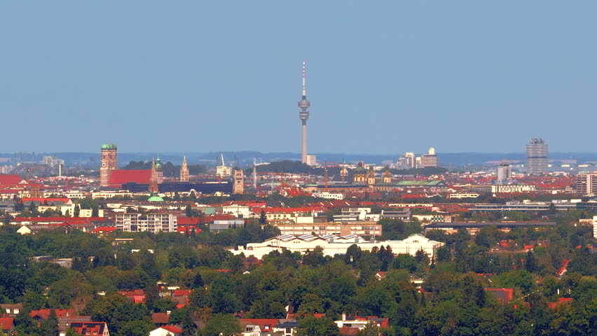 Aerial panoramic view of the Munich skyline featuring the Olympic Tower, historic landmarks and the sprawling Bavarian capital beneath a clear blue sky in Germany.
