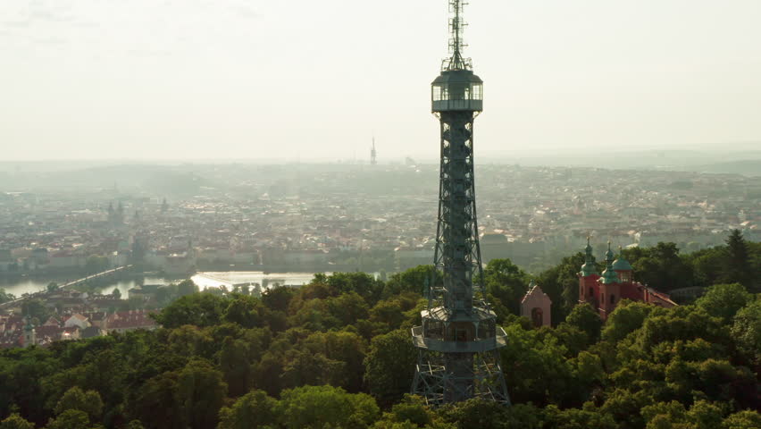 Panoramic view opens from Petrin Lookout Tower over Prague city center. Scenic vista reveals Vltava River, historic bridges and Prague Castle. Famous landmark attracts European travelers.