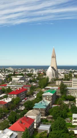 An aerial view of Reykjavik, Iceland on a sunny day. The cityscape features the iconic Hallgrímskirkja church, colorful rooftops, and the North Atlantic Ocean in the background.