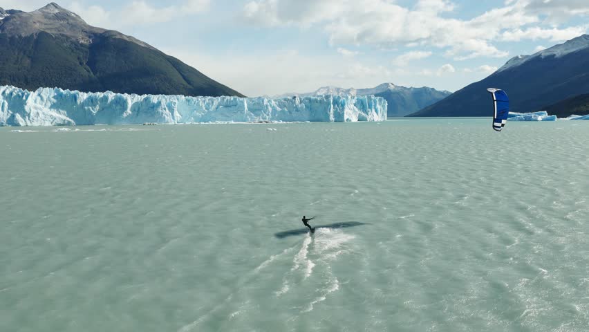 Drone follows a kitesurfer across Lago Argentino near Perito Moreno Glacier, El Calafate, Santa Cruz, Argentina, with floating icebergs and the glacier front stretching across the horizon drone follow