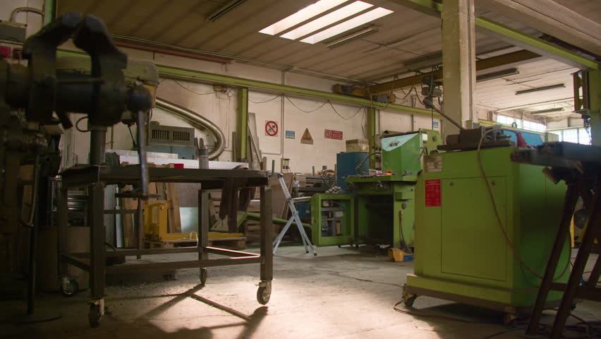 Blacksmith workshop tools illuminated by skylight sunbeam, handheld wide shot. Interior of a traditional forge garage filled with industrial machinery.