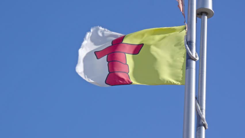 Cinematographic slow-motion telephoto shot capturing the detailed movement of the Official Nunavut Flag as it ripples in the wind against a clear blue sky.