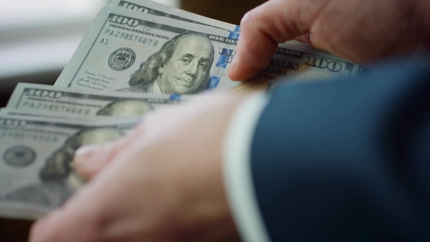 Close-up of hands counting three hundred dollar bills featuring blue stripe and portrait of Benjamin Franklin. Indoor setting with soft light creates a clear view of the money.