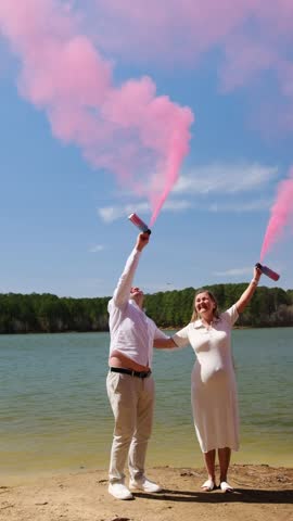 Expecting couple celebrating gender reveal with pink smoke