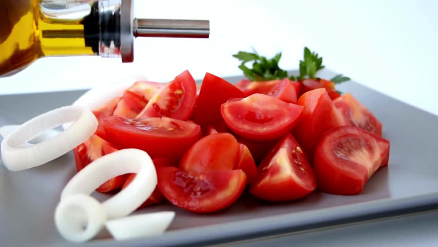 A salad of fresh sliced Tomatoes and Onion Rings is on a Grey plate. Olive oil is poured on top. A close up. Culinary concept.