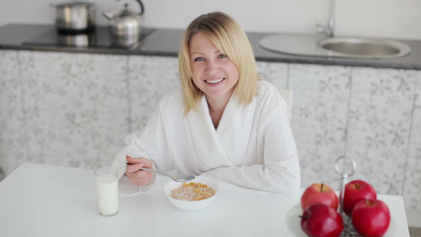 Woman in bathrobe sitting at table and eating breakfast
