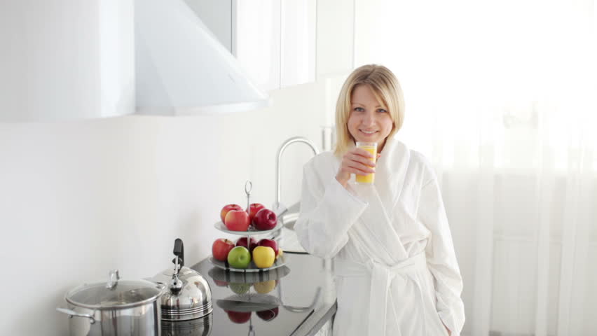 Woman in bathrobe comes into kitchen and drinking juice

