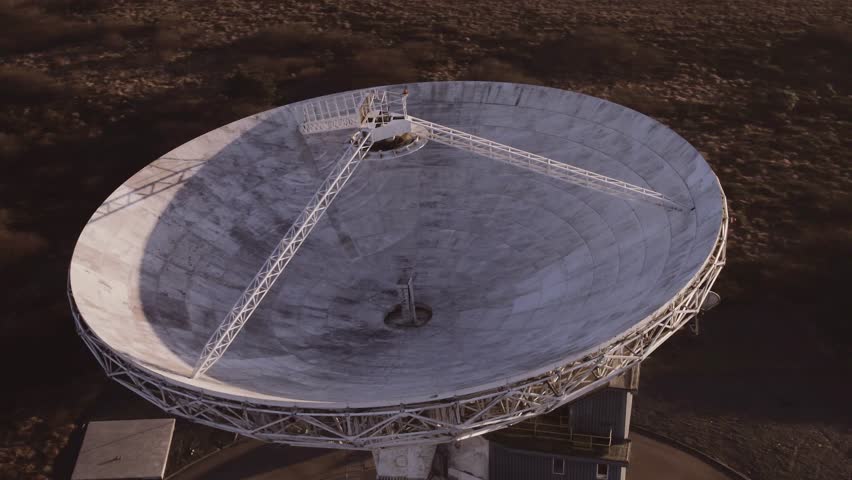 A large radio telescope dish rotates in the desert at sunset, providing a vital communication link for deep space research and exploration.