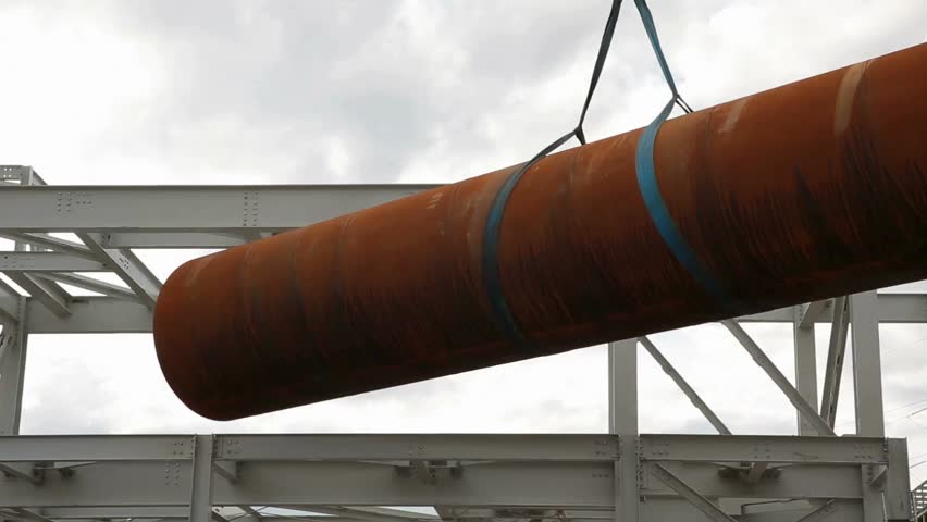 Heavy machinery lifts steel pipe for construction project at industrial site machinery in action against a backdrop of a cloudy sky, emphasizing engineering processes in development.