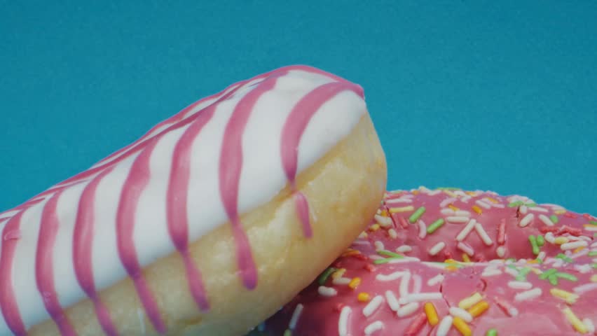 Two donuts, one with pink sprinkles and one with pink stripes, are positioned against a bright blue backdrop. Focus is on the sweet dessert treats.