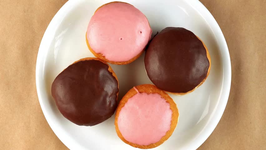 Four donuts with chocolate and pink frosting sit on white plate. Delicious treat is shot overhead. Tasty snack ready to eat.