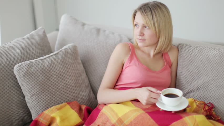 Woman relaxing on couch under blanket and drinking hot coffee
