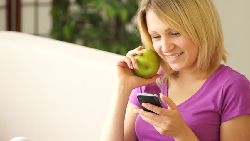 Lovely girl holding phone and an apple and laughing
