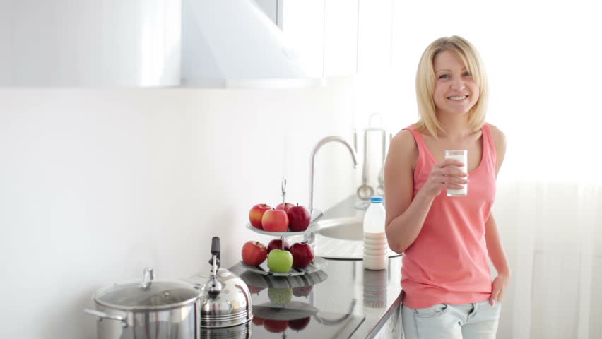 Girl standing in kitchen drinking milk with smile
