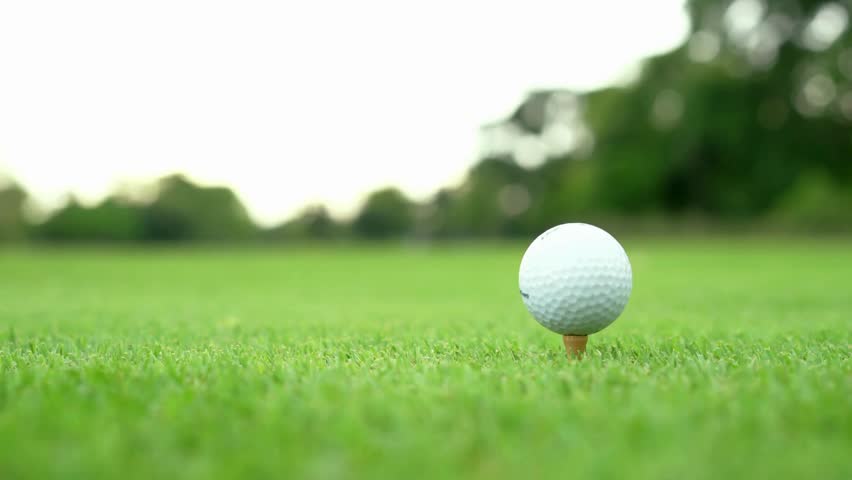 Golfer approaches ball on tee while preparing to take a swing. Grass is vibrant and green, with soft sunlight illuminating the scene, creating a serene atmosphere.