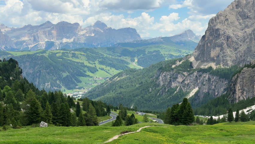 Breathtaking panoramic view of the italian alps with a winding road crossing a verdant valley