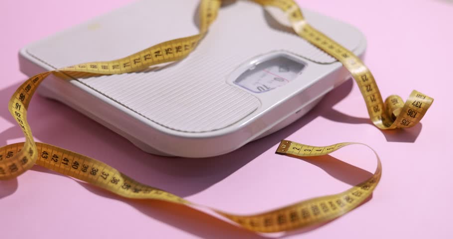 Scales with measuring tape on pink background, closeup. Camera moving in