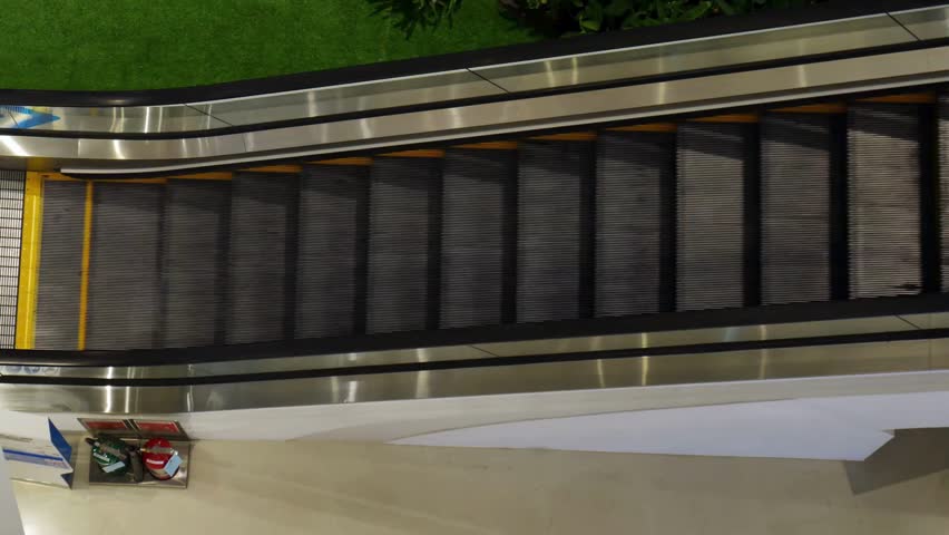 High-angle view of a modern indoor shopping mall escalator with clean architectural design and greenery, ideal for commercial retail backgrounds.