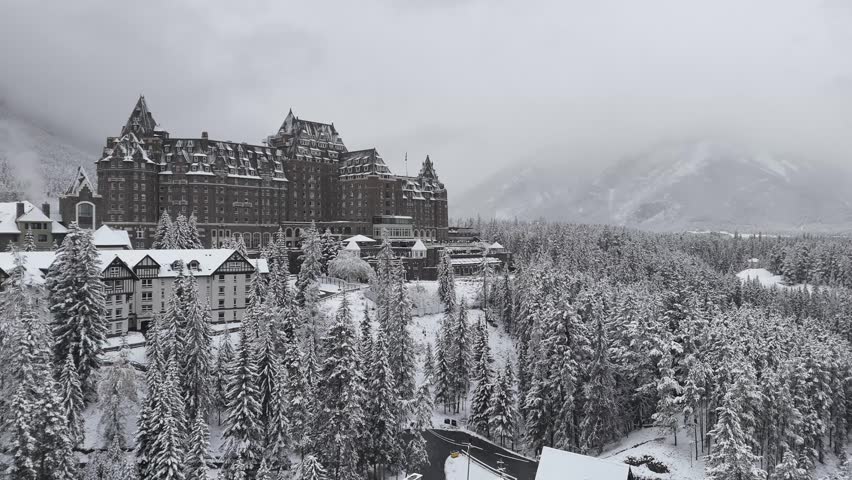 Aerial view of the iconic Fairmont Chateau Lake Louise nestled amidst snow-covered evergreen forests and majestic rocky peaks during the winter season in Banff National Park, Alberta, Canada.