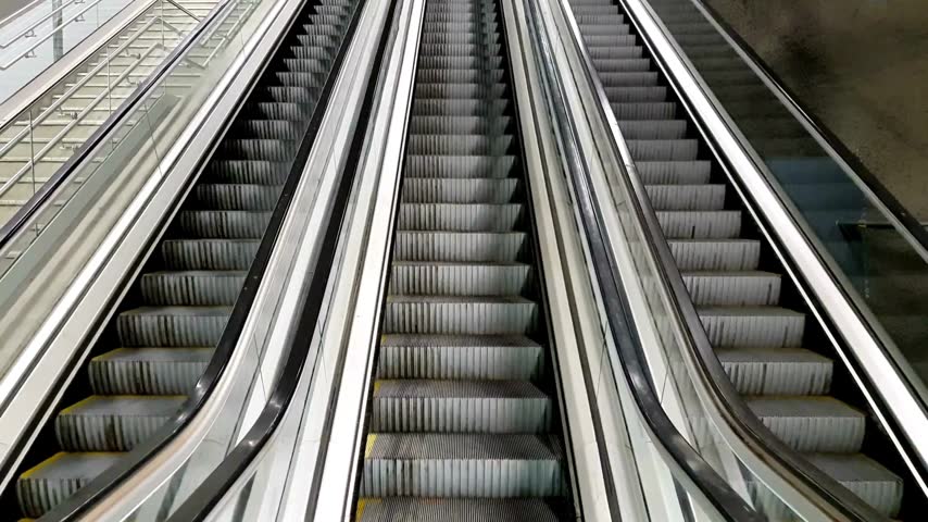 Ascending escalators in a modern, glass-railed shopping mall represent urban transit and commercial architecture.