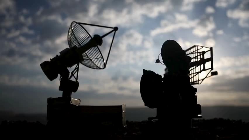 Silhouetted communication and radar dishes stand against a dramatic golden hour sky, highlighting massive metal structures designed for radio transmission and satellite tracking.