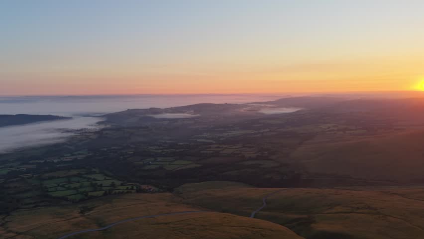 Atmospheric Sunrise in South Wales with Sprawling Farmed Fields and Moorlands of Brecon Beacons with Mist Filling Low Lying Terrain Below.