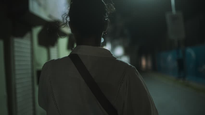 Person walks alone down a dimly lit street at night, passing closed storefronts