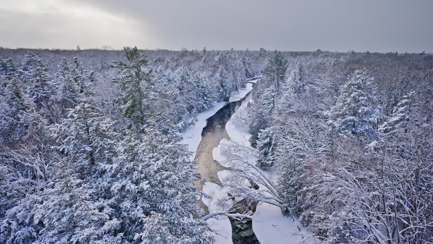 Winter aerial of a river flowing through untouched snow in Northern Michigan.