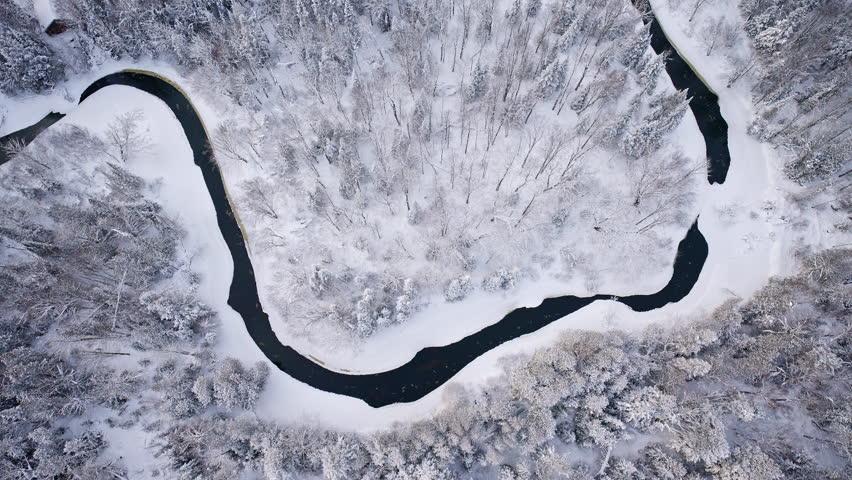 Cinematic drone footage of a tranquil river surrounded by an enchanting snowy landscape in Northern Michigan.