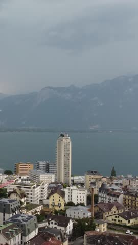 Vertical video of a lightning strike over the mountains behind Montreux and Lake Geneva in Switzerland during a storm, with city buildings, lake and alpine landscape in view.